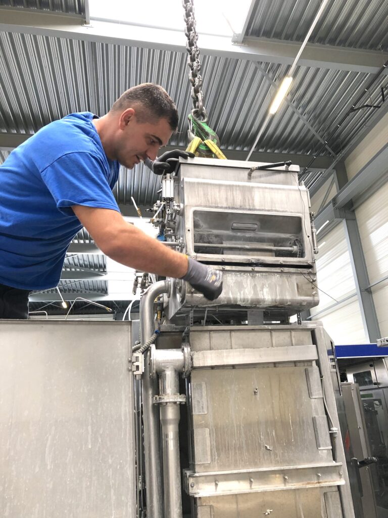 Techniker in Arbeitskleidung montiert ein Bauteil an einer Maschine in der Werkstatt